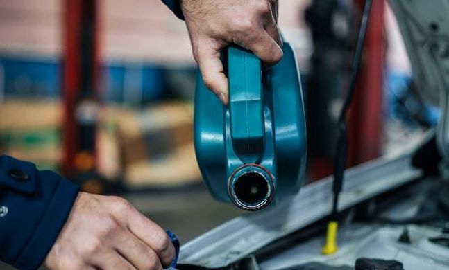 Technician pouring oil from a teal container
